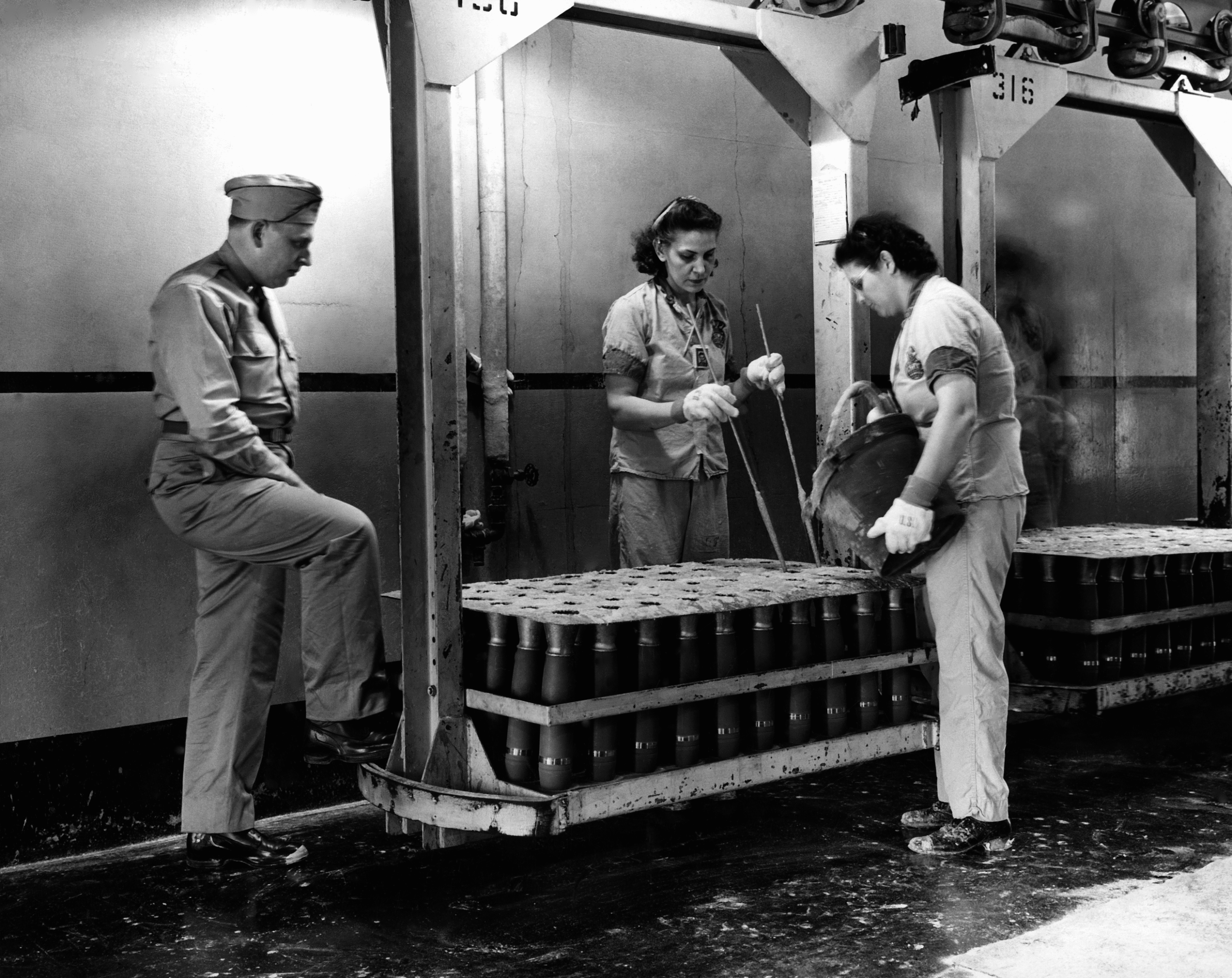 PHS dermatologist Donald Birmingham observes two ordnance workers pour TNT into mortar shells at the Ravenna Ordnance Plant in 1943, as part of the Division of Industrial Hygiene's efforts to prevent TNT poisoning and other diseases during World War II.