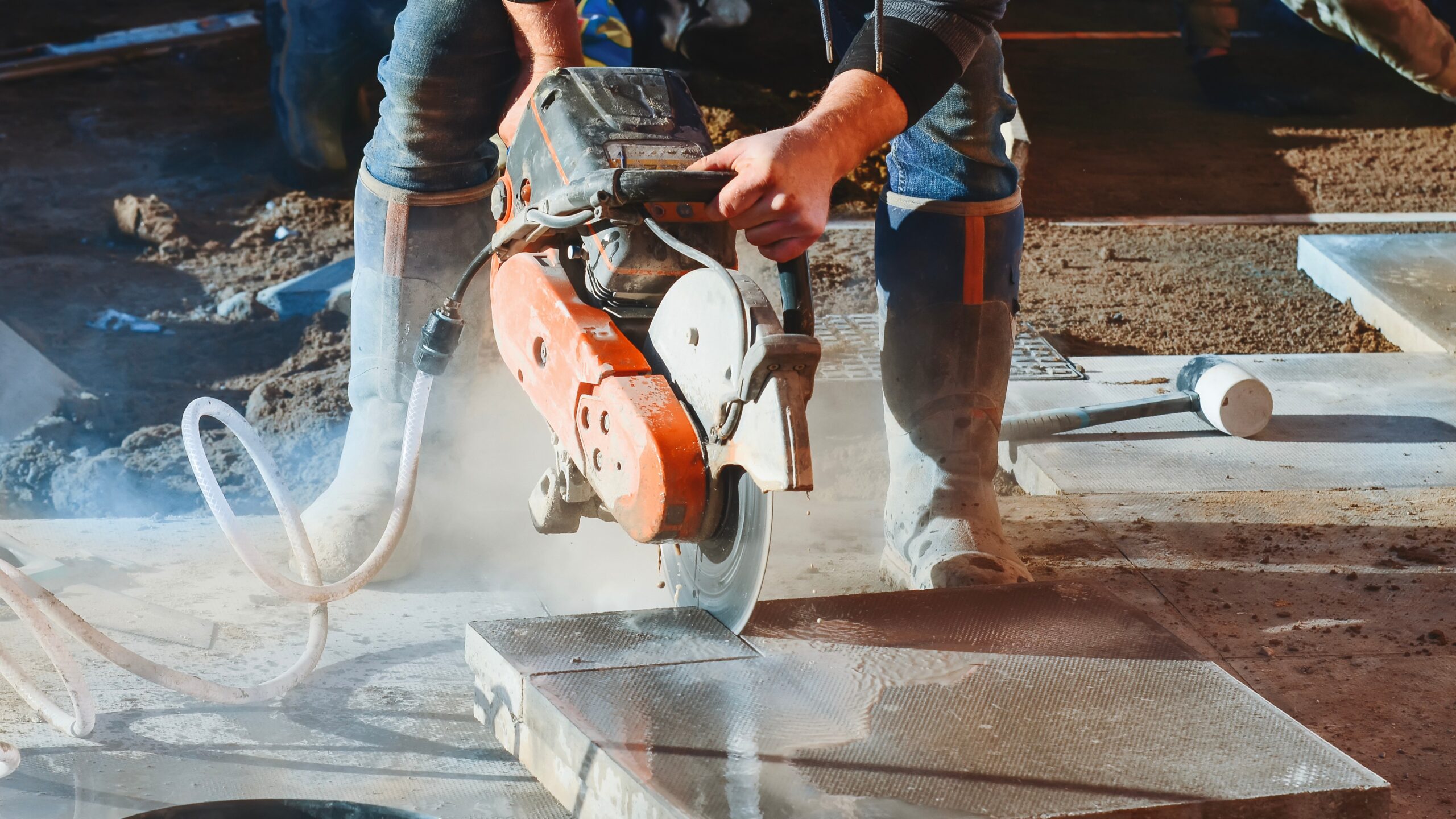 Construction worker cutting concrete paving tiles with concrete cutter saw and water dust suppressor