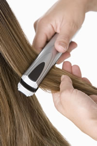 A stylist uses a silver flat iron on long, dark blonde hair.
