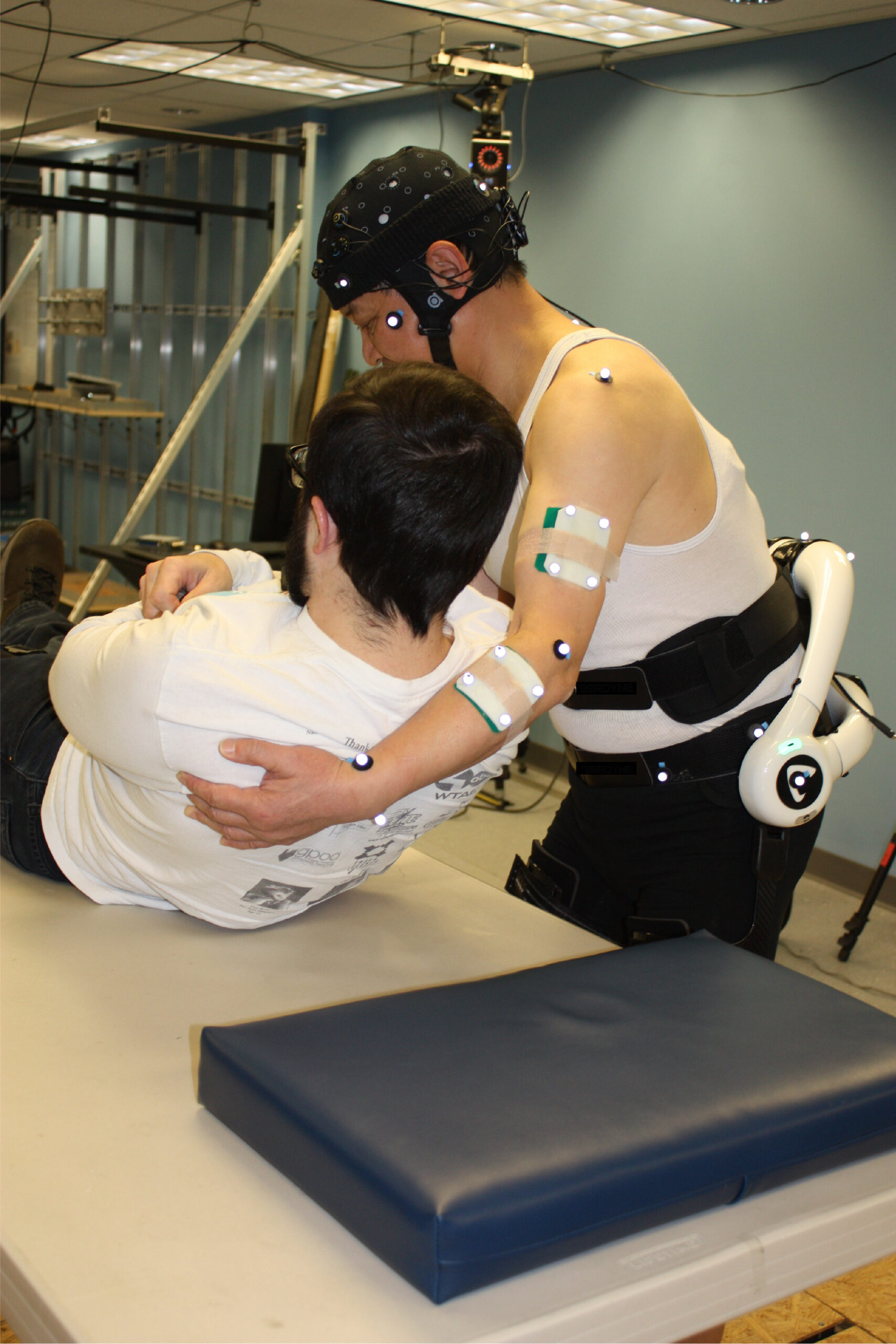 NIOSH researcher wears a powered back-assist exoskeleton while performing a pilot test on a “patient” volunteer