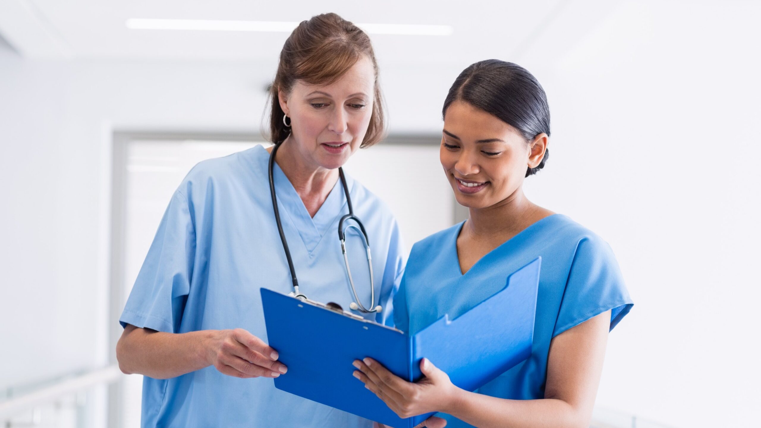 Two nurses looking at a file together, standing in a hall