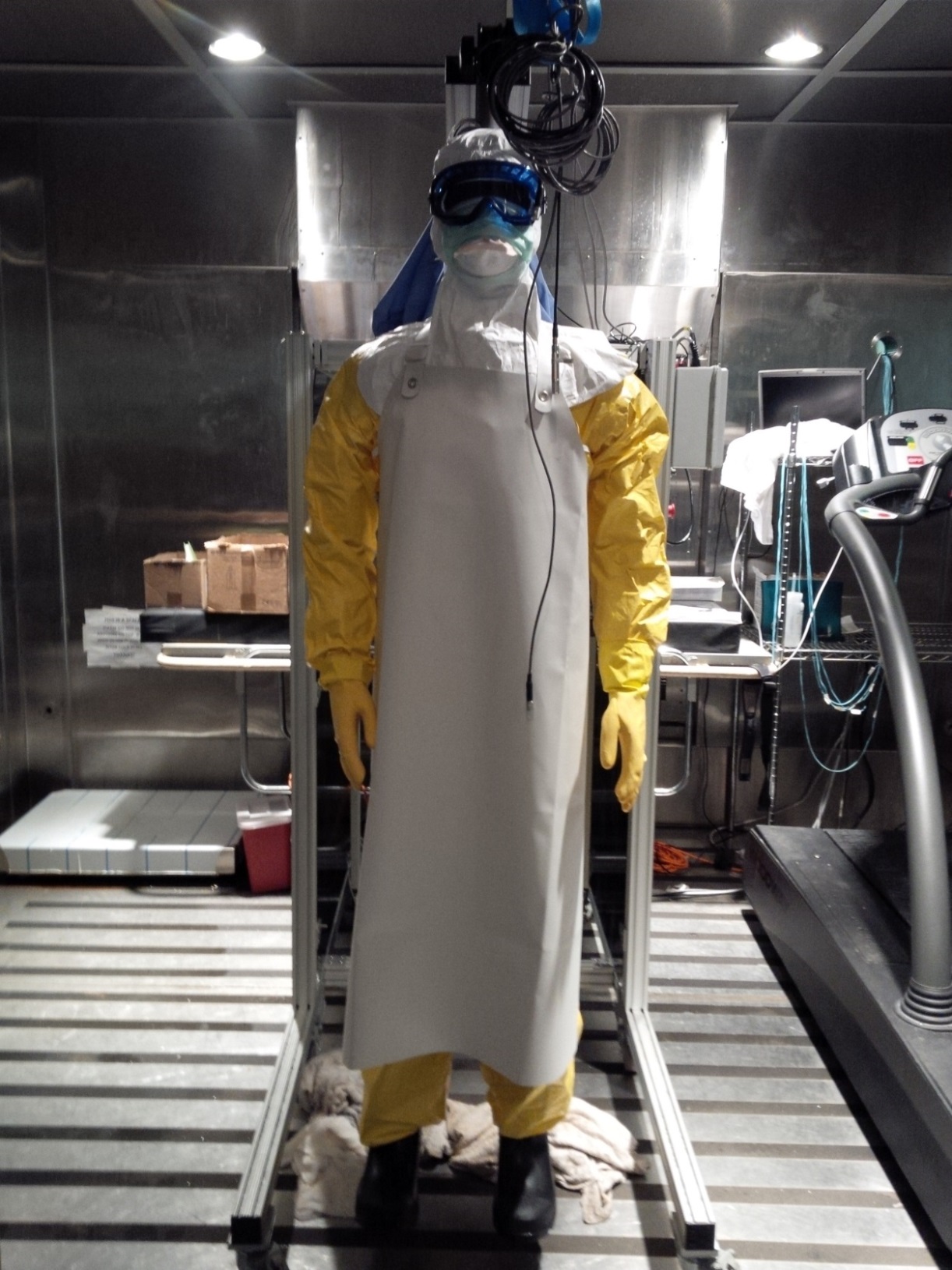 A person wearing head-to-toe personal protective equipment, including coveralls, hood, mask, rubber apron, and boots.
