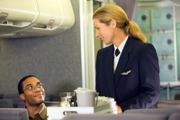 Female flight attendant walking with a cart, smiling at a passenger