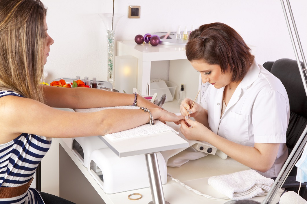 Nail salon worker at their desk painting a woman's nails.