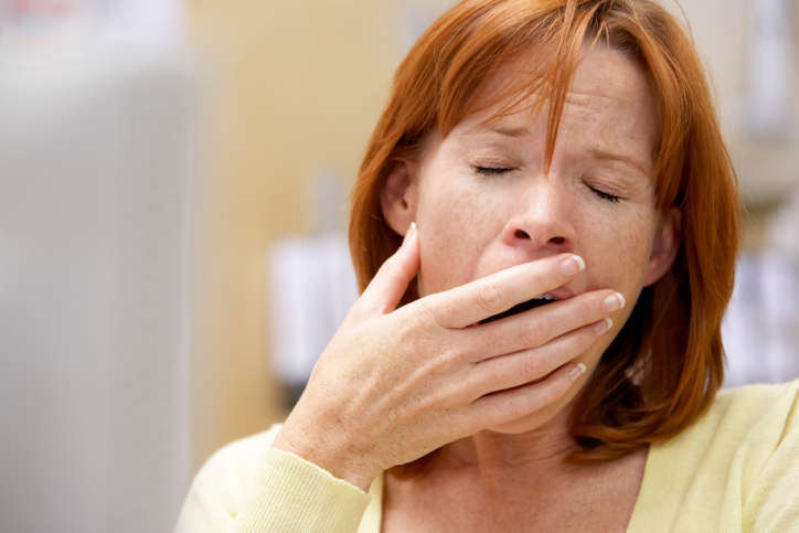 Woman with red hair wearing a yellow shirt and yawning.