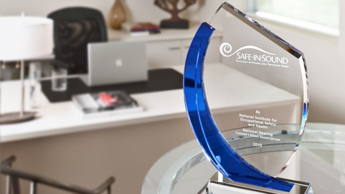 A glass trophy engraved with Safe in Sound on a table in an office.