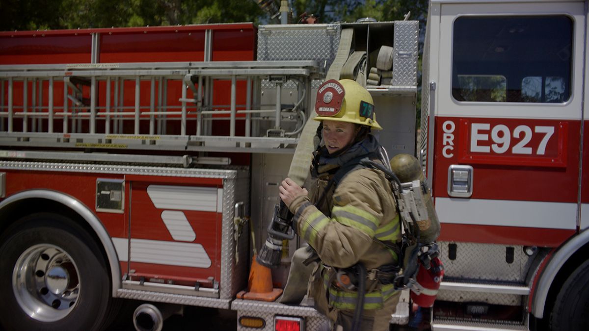 An OCFA firefighter carries a hose from a firetruck.