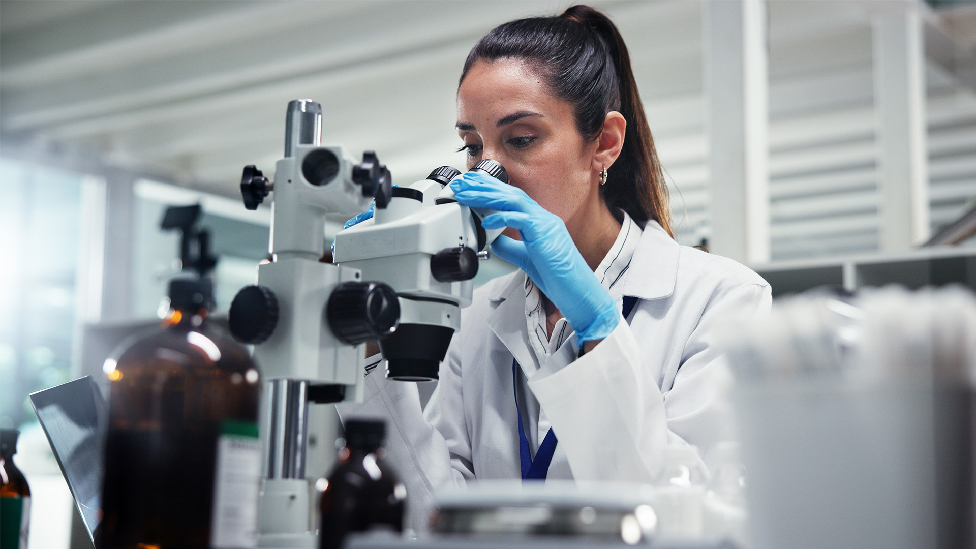 Female scientist wearing a lab coat and gloves using a microscope.