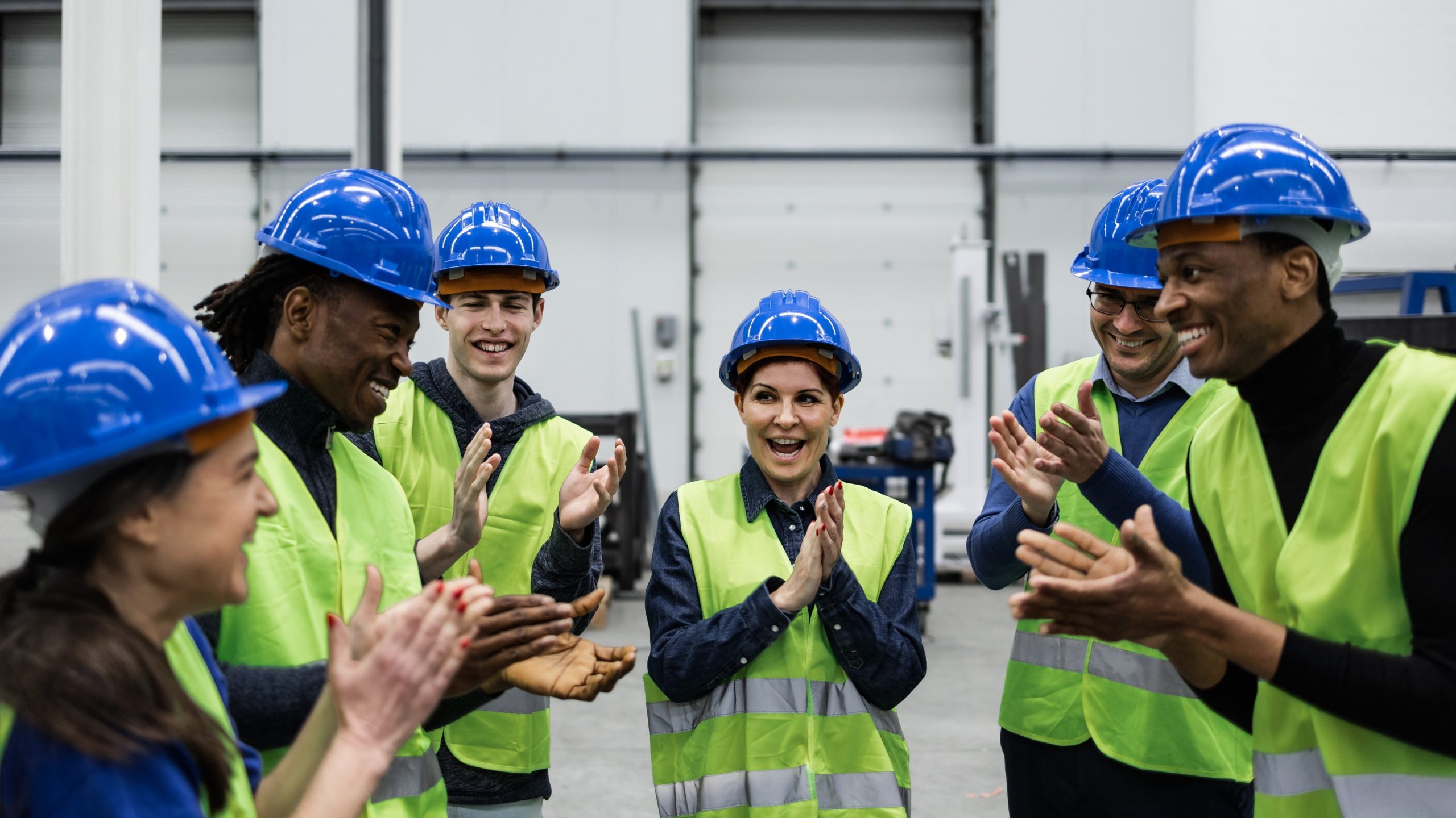 Team of Engineers Working in Robotic Factory A group of young adults standing in a half circle in safety vests and hardhats.