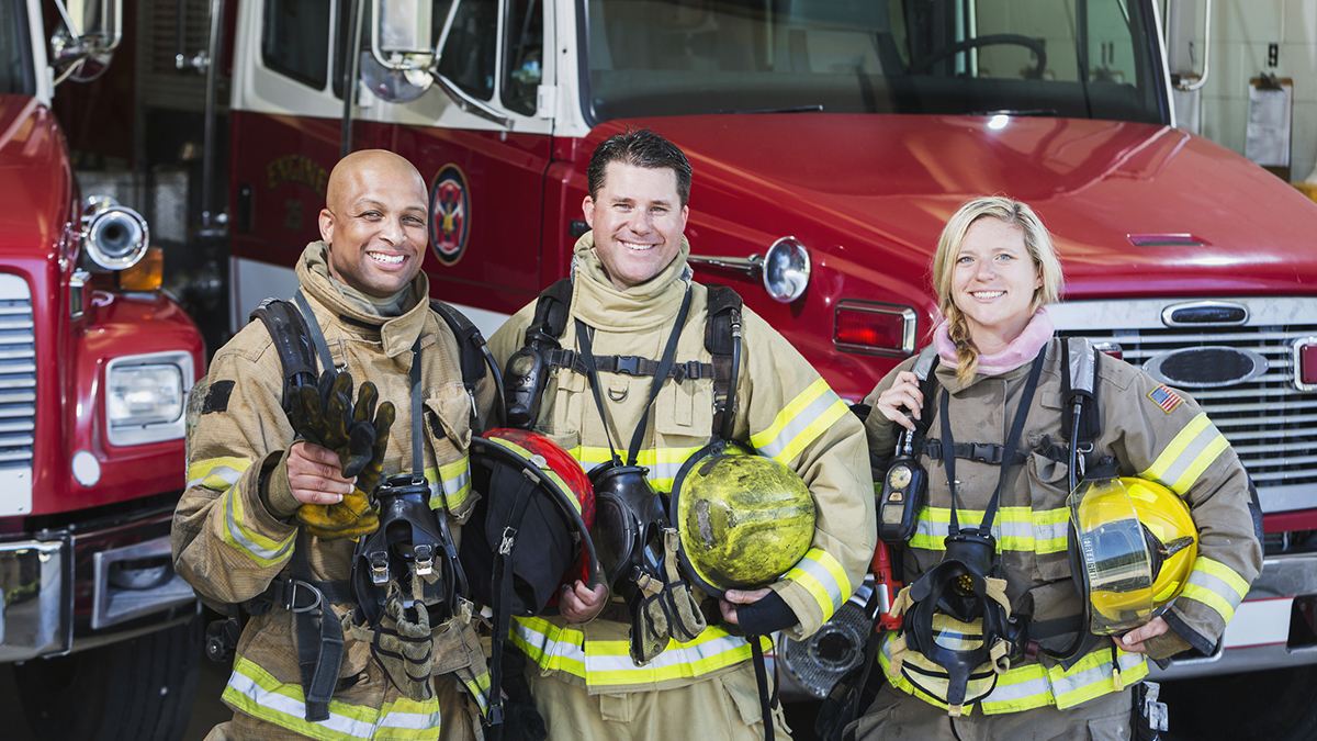 Group of structural firefighters standing in front of trucks with gear