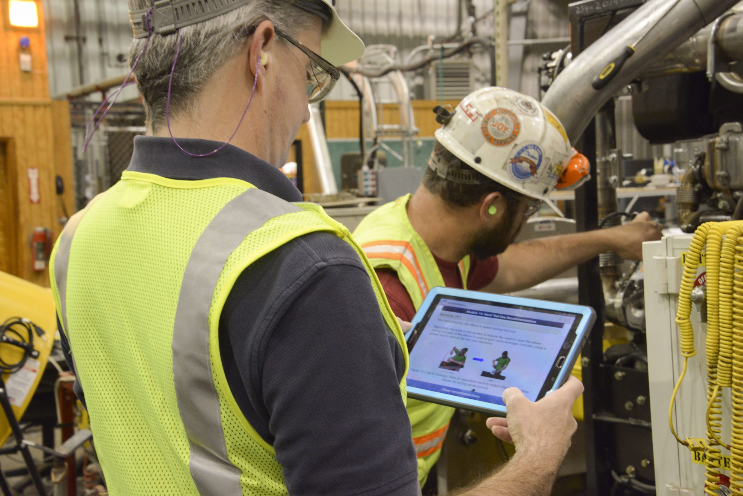 Two workers use the ErgoMine 2.0 mobile app to conduct an ergonomics audit during an equipment maintenance task. Photo from NIOSH.