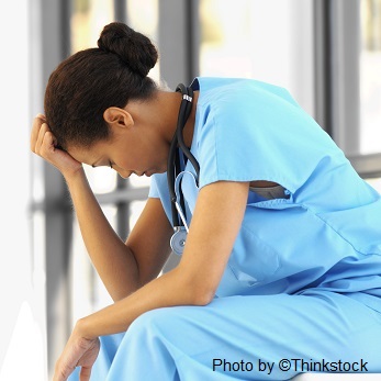 A nurse sits with her hand on her forehead