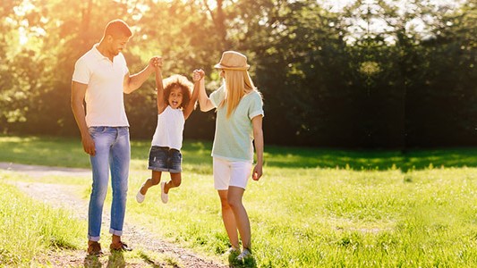 — title missing — Couple with young child walking in a park on a sunny day.