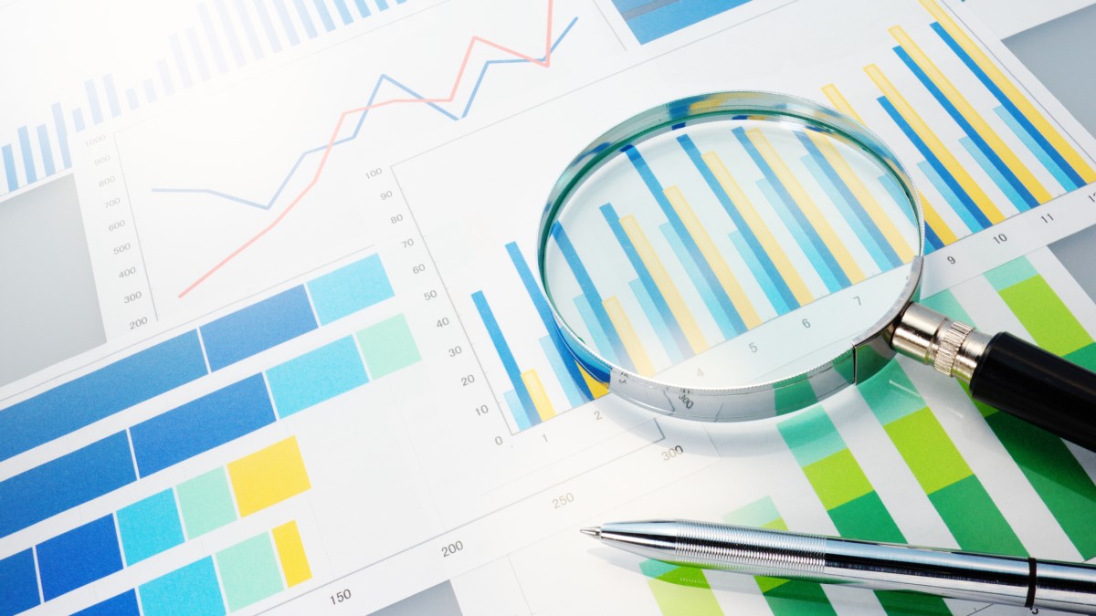 Magnifying glass and pen on top of paper with bar charts and line graphs.