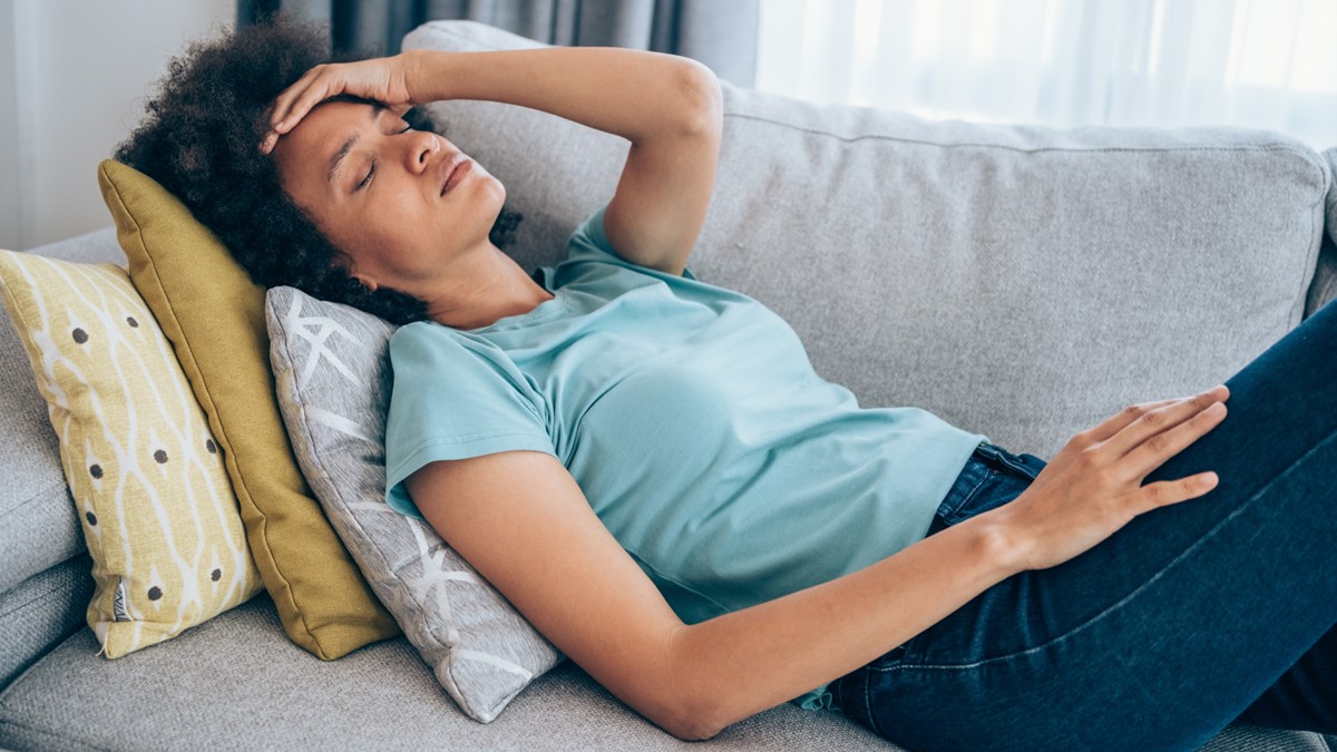 Photo of a sick woman with a headache and is resting on the couch.