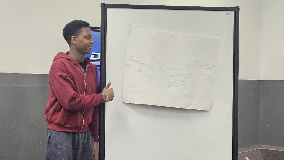 Adolescent standing in front of a drawing on a white board.