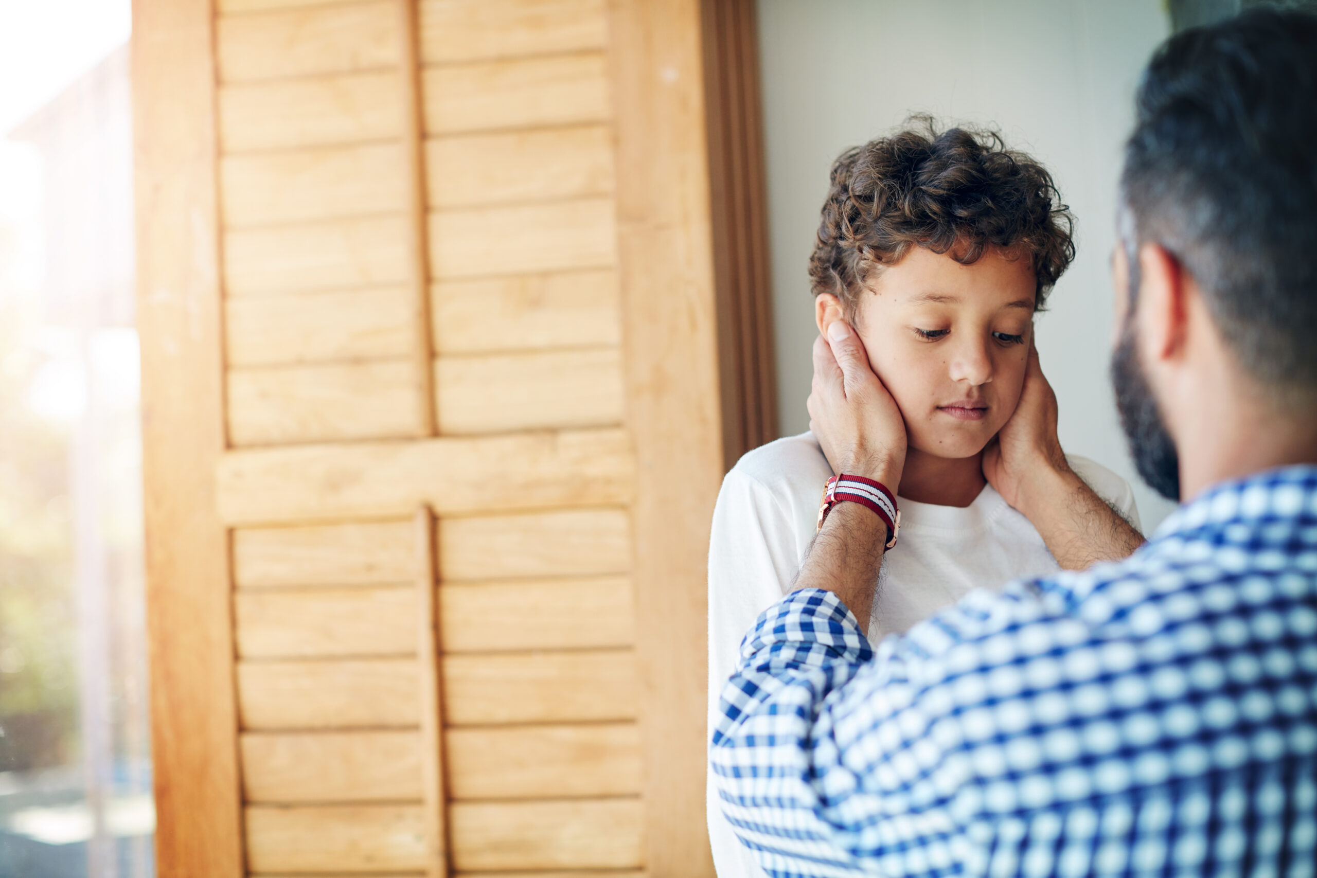 Dad gently holding a young boy's face as the boy looks down