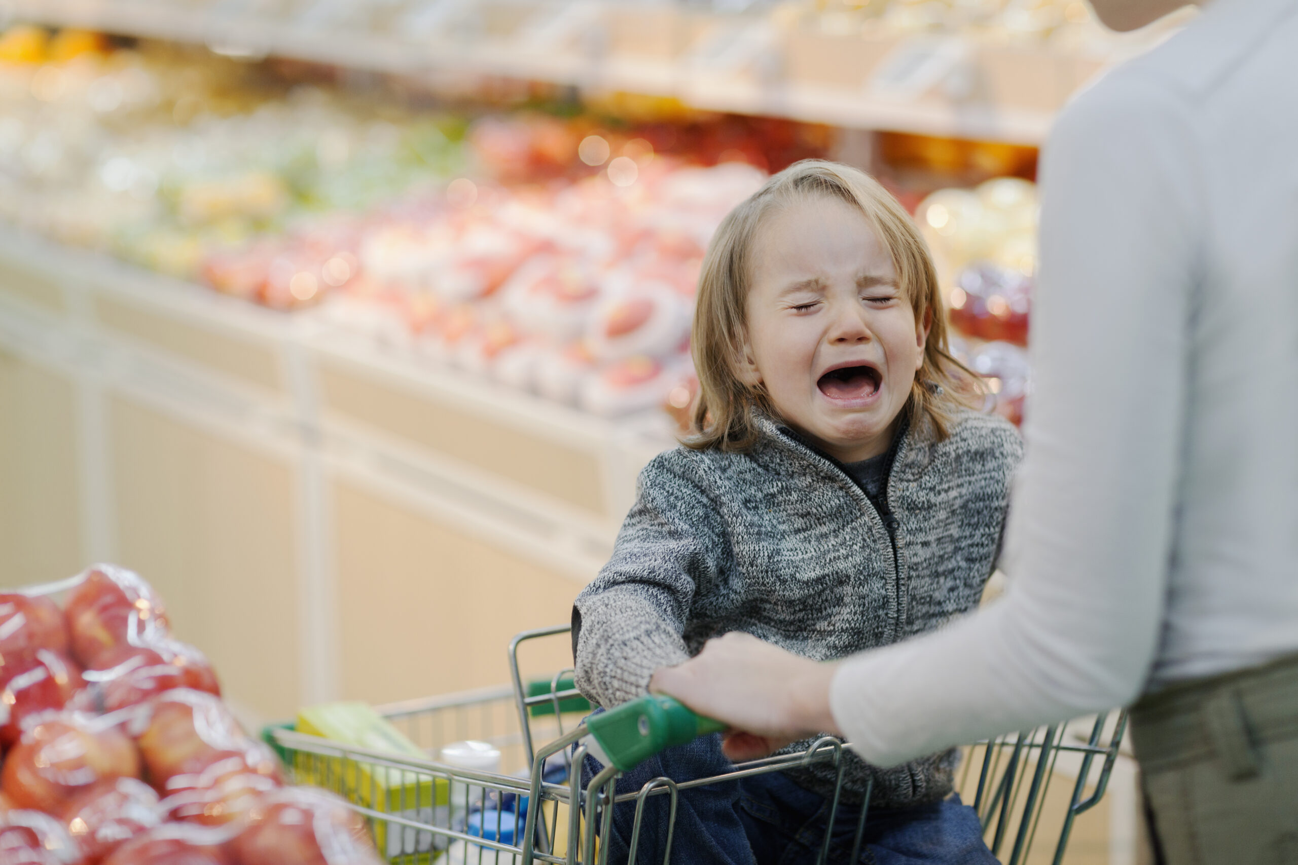Toddler child crying while sitting in a grocery cart being pushed by the parent