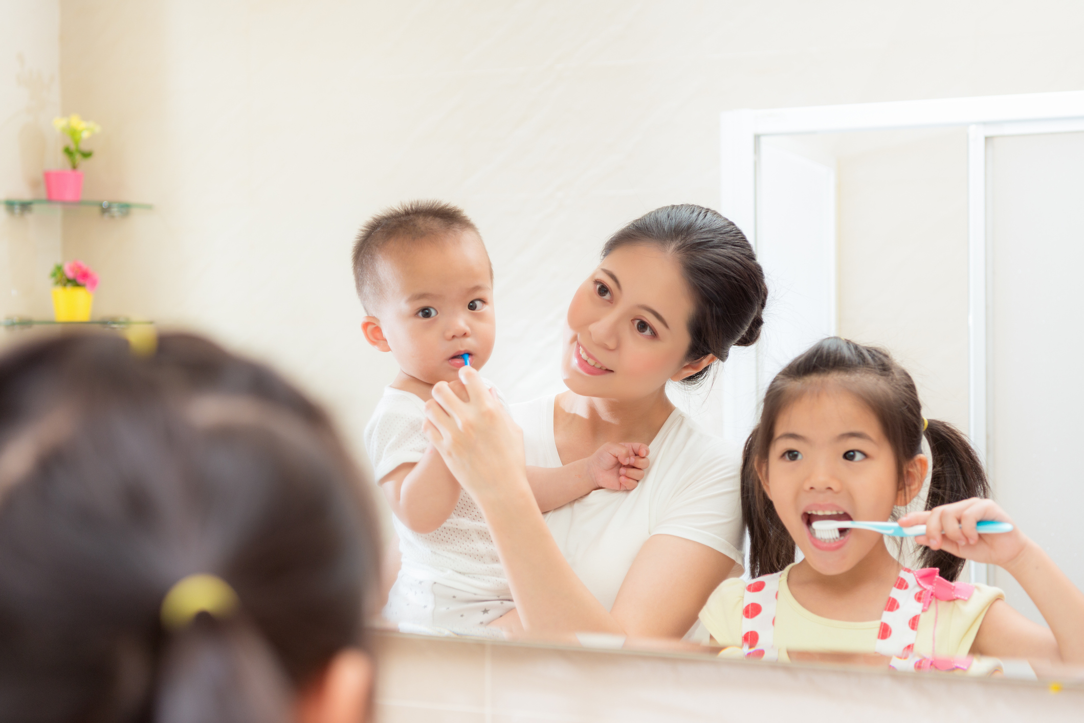 Mom helping two young children brush their teeth