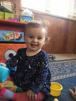 Toddler sitting upright on floor wearing blue shirt
