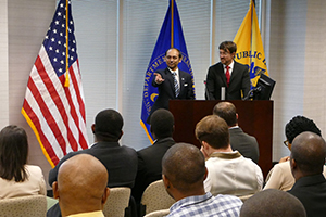 Two men wearing suits standing at a lectern speaking in front of an audience.