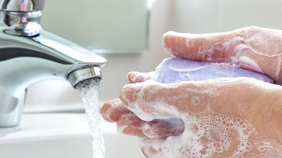 stay healthy Close-up of white hands lathering with a bar of soap next to running water of a bathroom sink faucet.