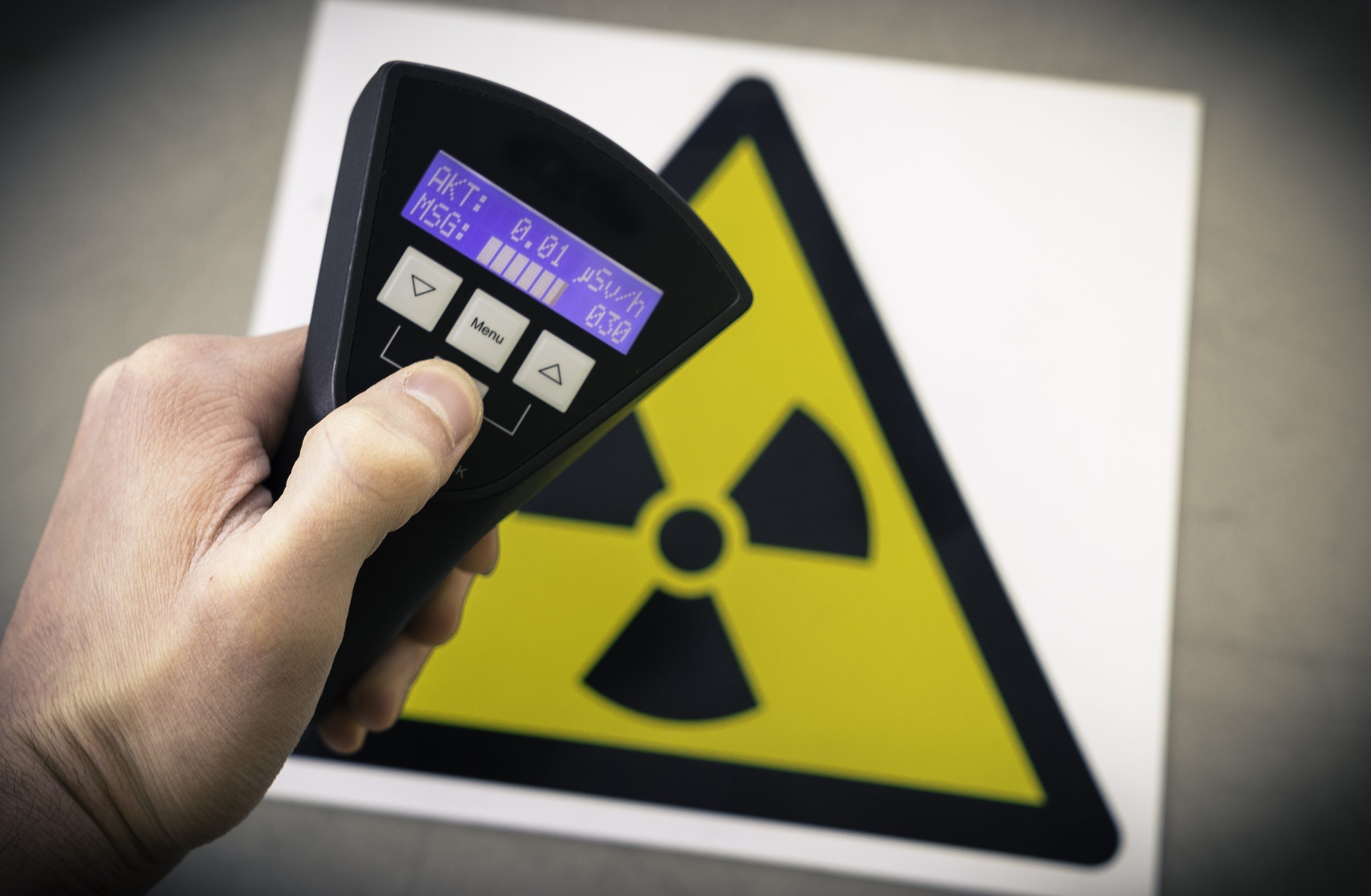 Measuring radiation levels Hand holding device to measure radiation levels. Sign with triangle radiation tri-foil symbol is in the background.