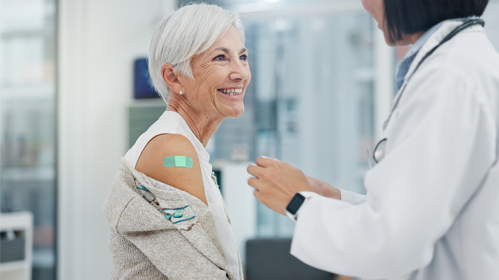An older woman with a Band-Aid on her arm after receiving a vaccine from a healthcare professional.