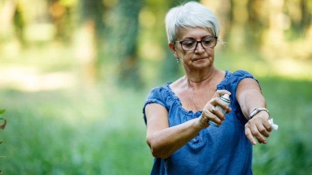 Older woman spraying insect repellent on her arm.
