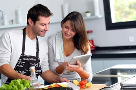 Pareja cocinando con ingredientes frescos en la cocina de su casa.
