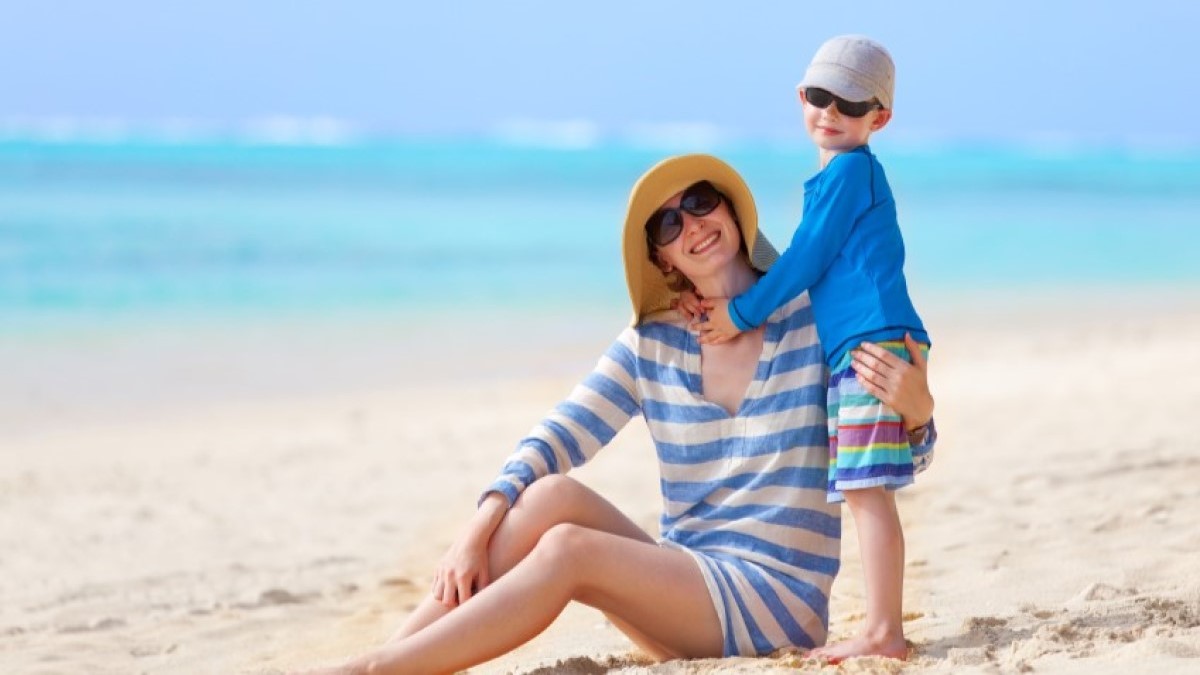 a mother and her young son wearing hats and sunglasses on the beach