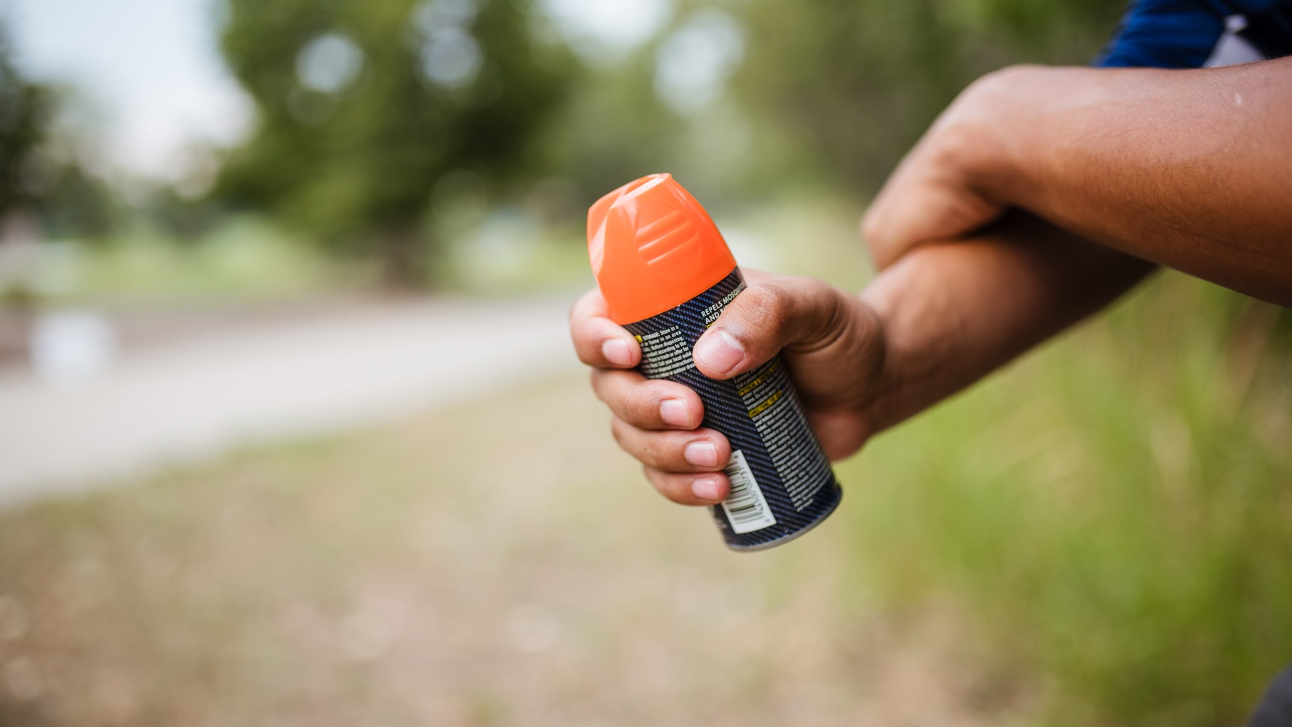 A person outside rubs insect repellent on their arm.
