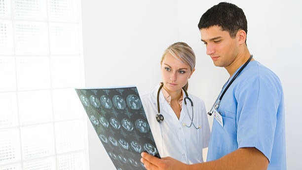 A female doctor and a male nurse look at a brain scan sheet.