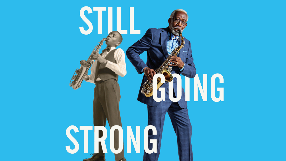 Older man playing the saxophone in foreground with younger version playing saxophone in the background. Still Going Strong.