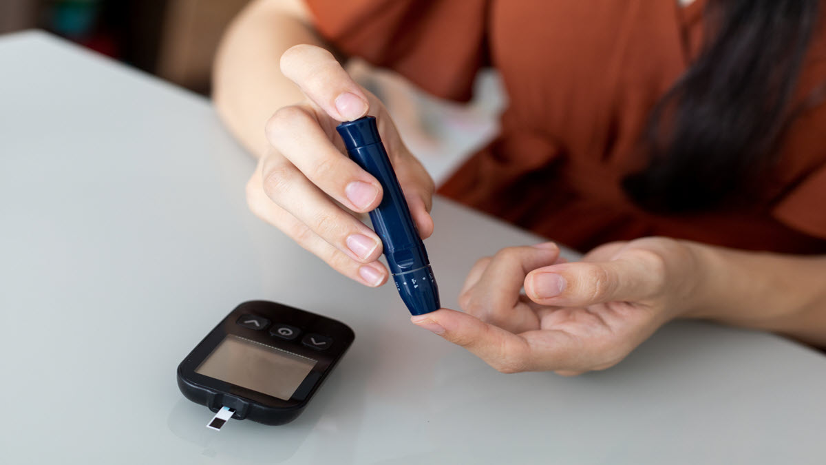 Diabetic patient, performing blood sugar level check by doing a finger-prick test. A person with diabetes performs blood sugar level check by doing a finger-prick test.