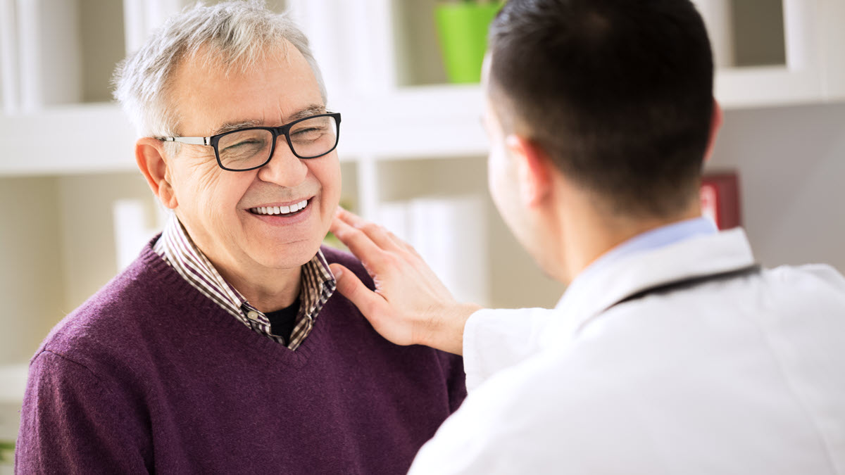 Un paciente con anteojos sonriendo mientras habla con un proveedor de atención médica.