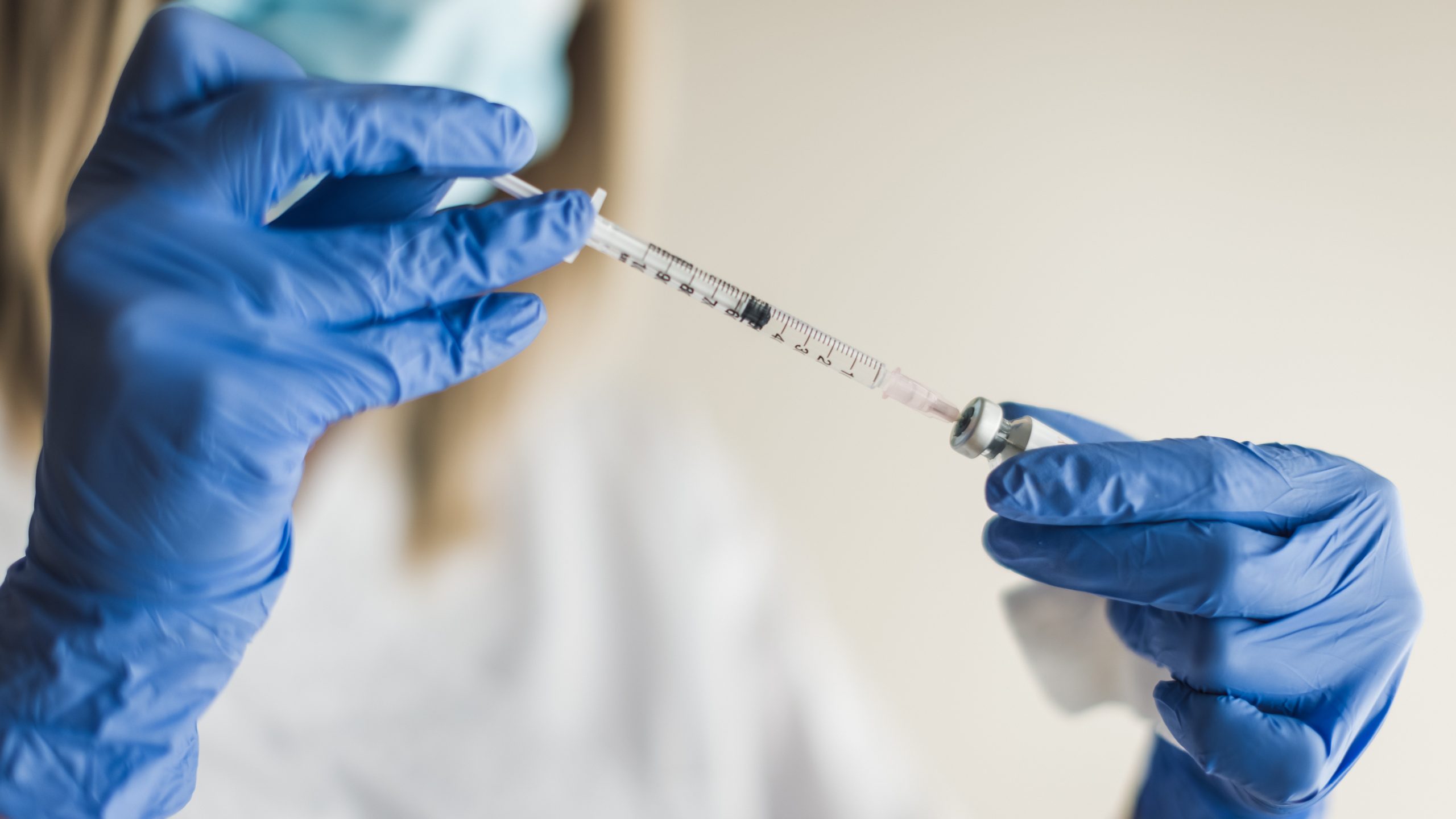 Healthcare professional inserting a syringe into a vaccine vial.