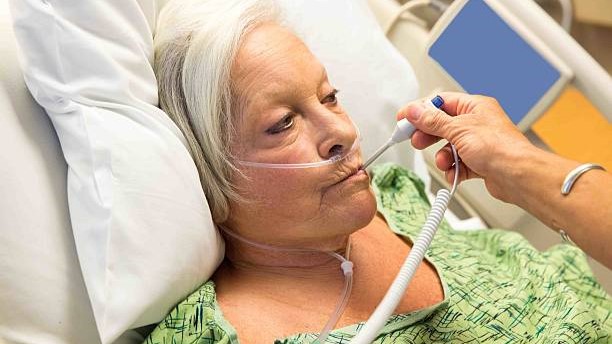 Older woman in a hospital bed getting her temperature taken.