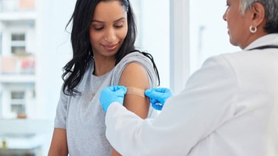A female physician applies a bandage to a woman who has received a vaccination.