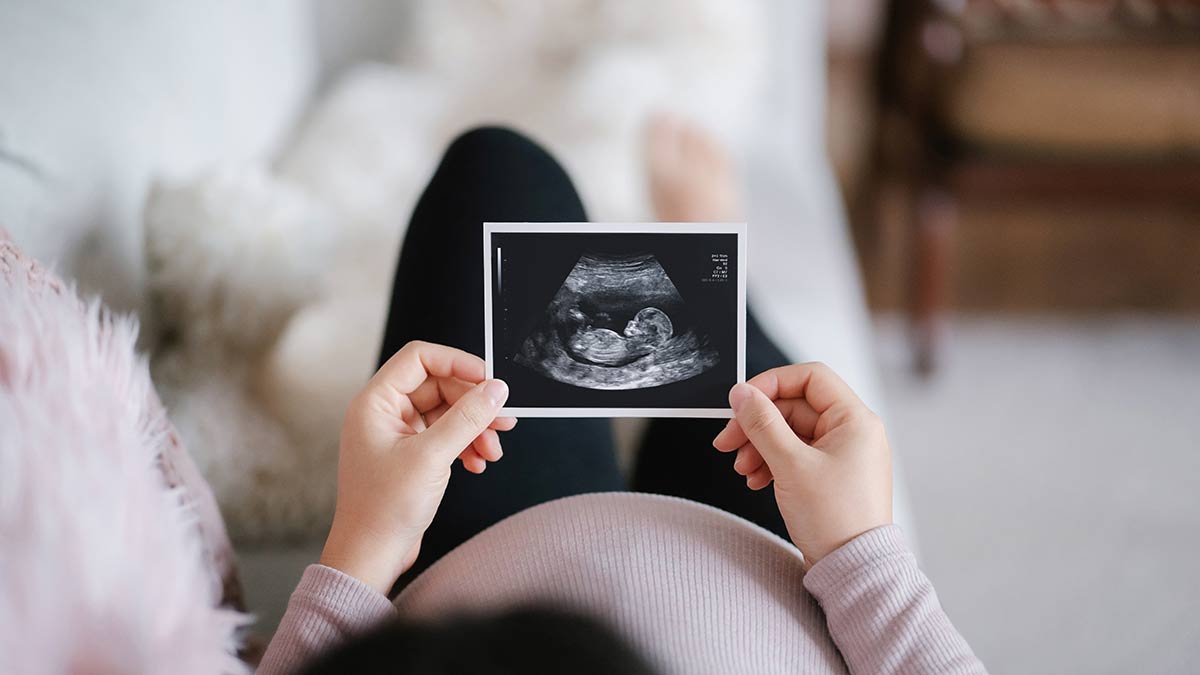 cdc-osh-woman-sonogram Pregnant woman lying on sofa at home looking at the ultrasound scan photo of her baby