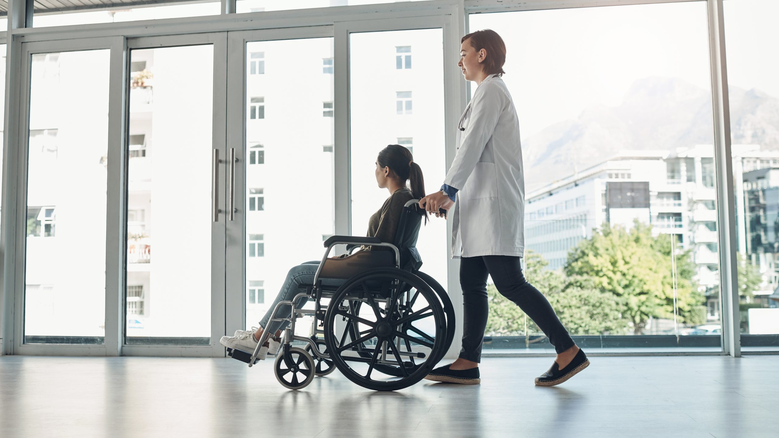 A healthcare provider pushes a patient in a wheelchar in a hospital
