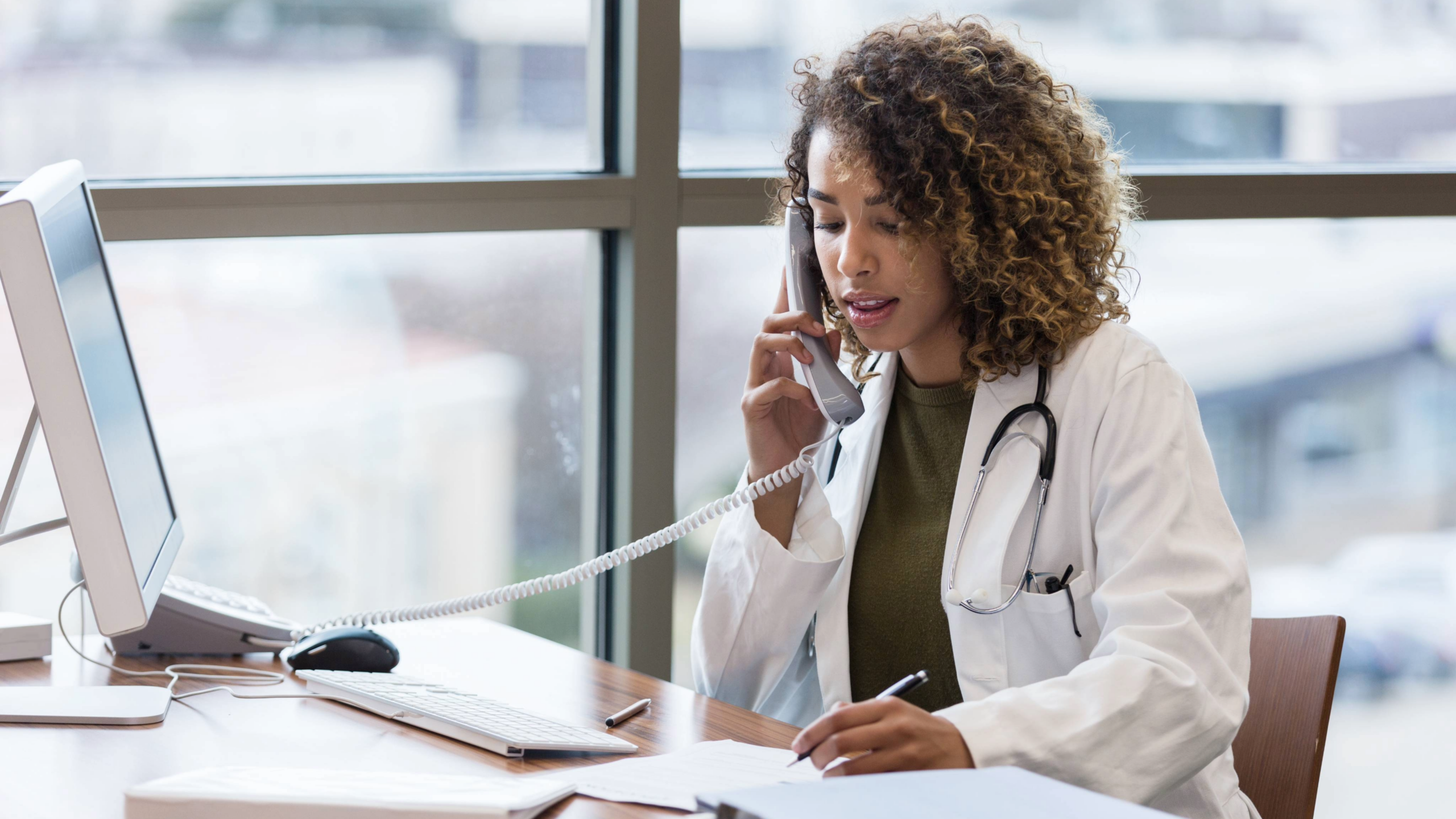 Female doctor talks on phone while sitting at desk