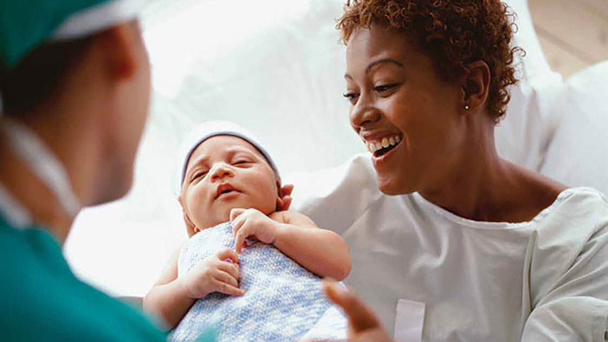 A mother smiles while holding her newborn baby in the hospital.