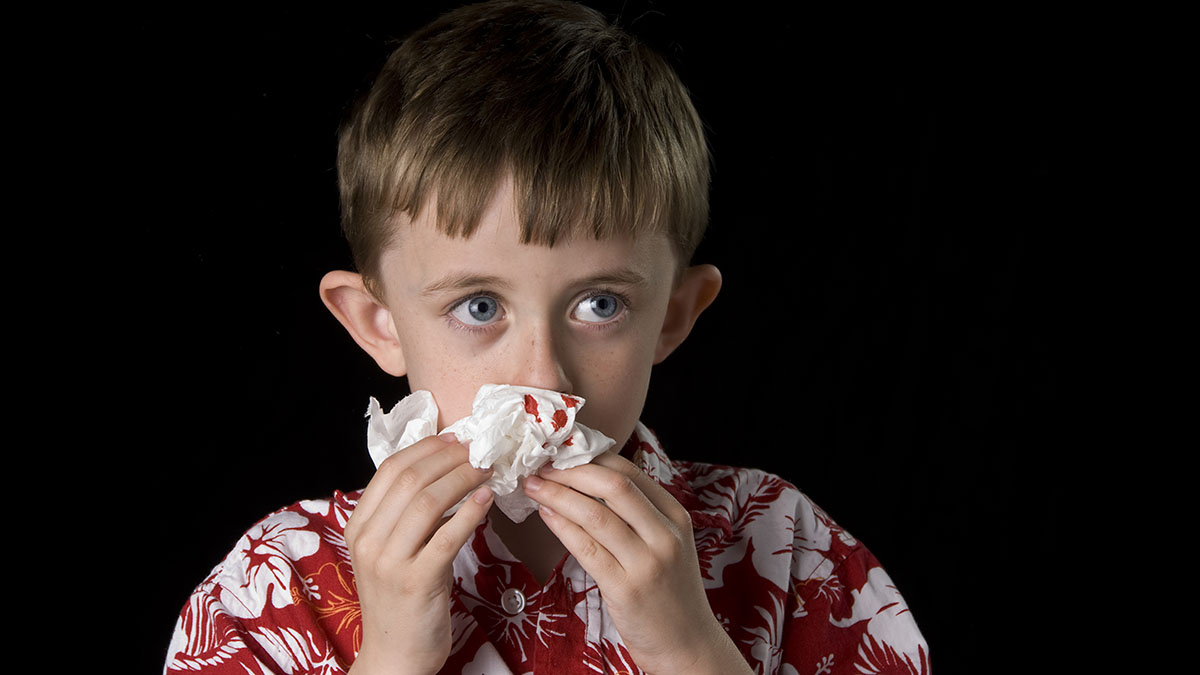Young boy blotting his nose with a tissue to help stop a nosebleed