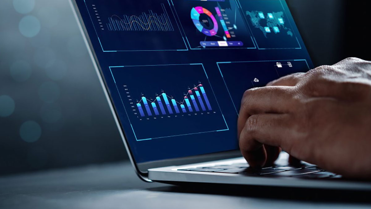 Image of a person's hands typing on a laptop displaying data charts and graphs.