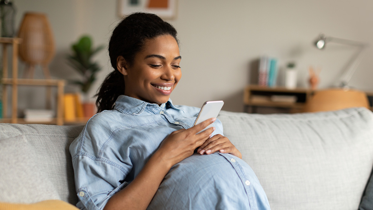 Happy pregnant mom-to-be Pregnant woman sitting on a sofa, smiling at her cell phone