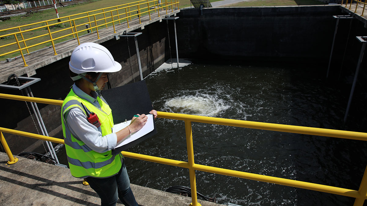 Un trabajador de aguas residuales, con equipo de seguridad, registra observaciones en un tanque de una planta de tratamiento.
