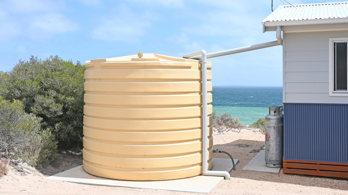 Tanque de almacenamiento de agua de pl&aacute;stico grande (cisterna) sobre una base de concreto. Un tubo de pl&aacute;stico conecta la cisterna a una manguera. Otro tubo de pl&aacute;stico va desde la cisterna hasta el suelo. Se ve que la cisterna y la casa est&aacute;n al lado del mar.