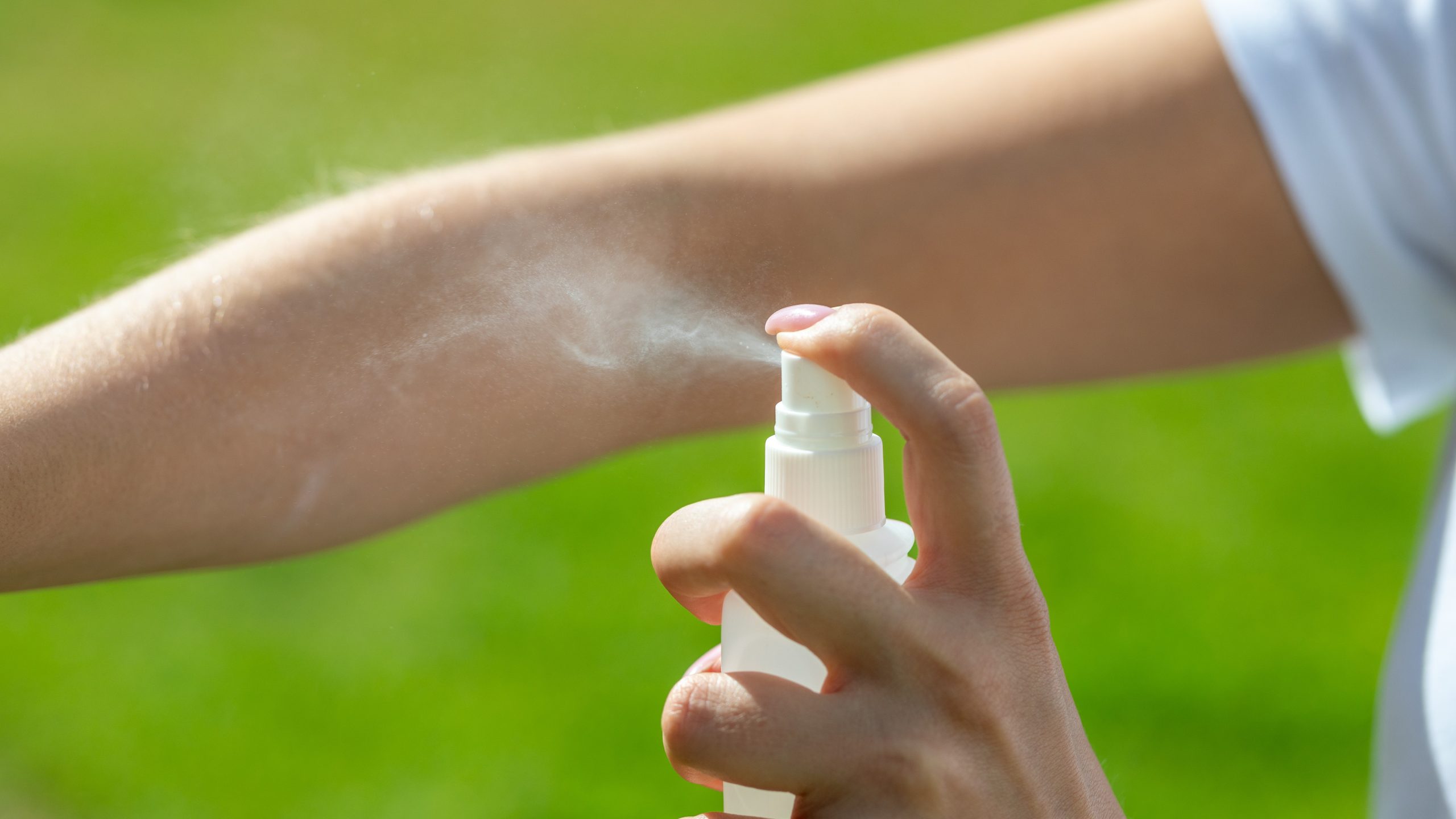 Person spraying insect repellent on their arm outdoors.
