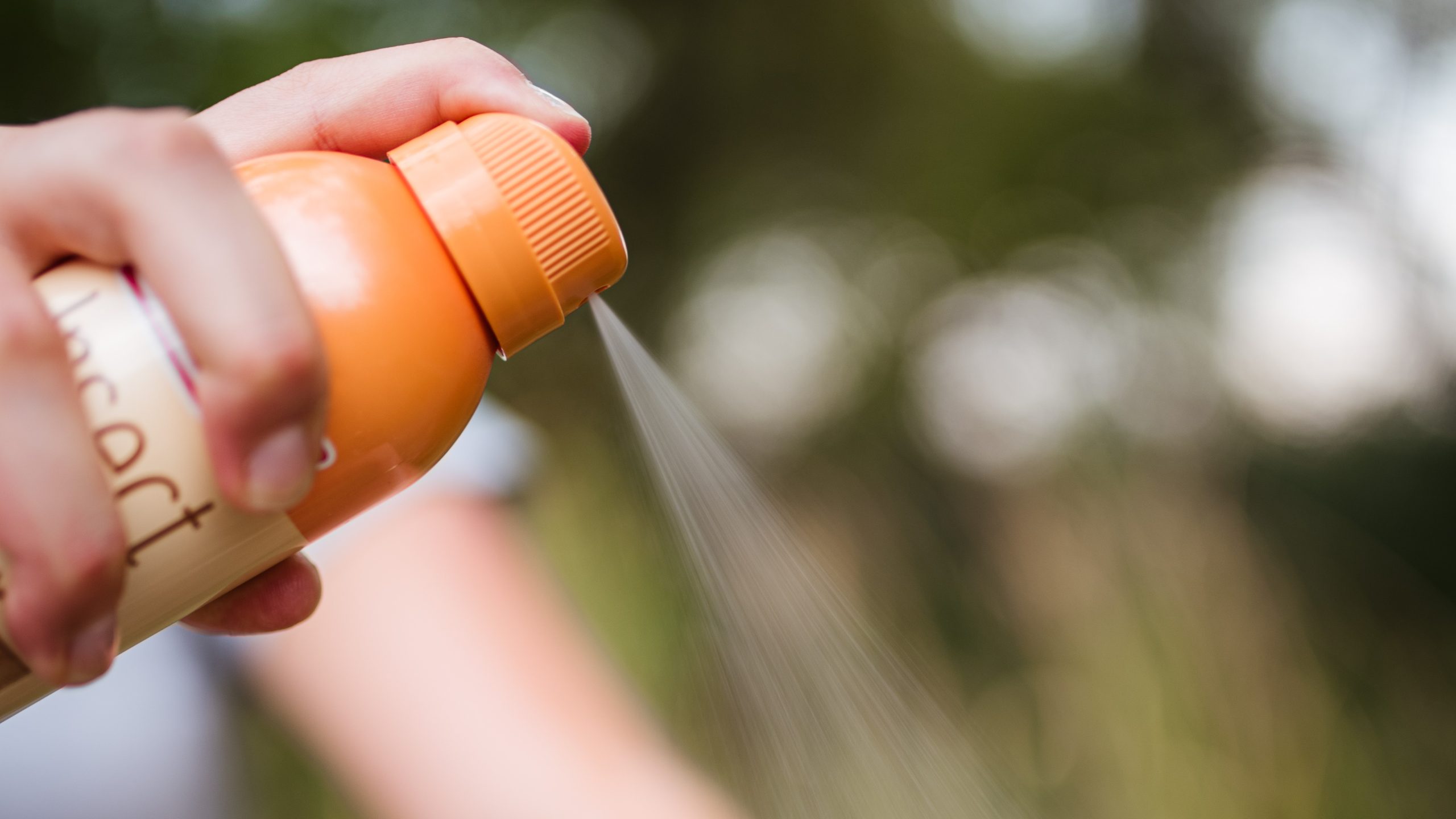 Person spraying insect repellent outdoors for prevention of bites.